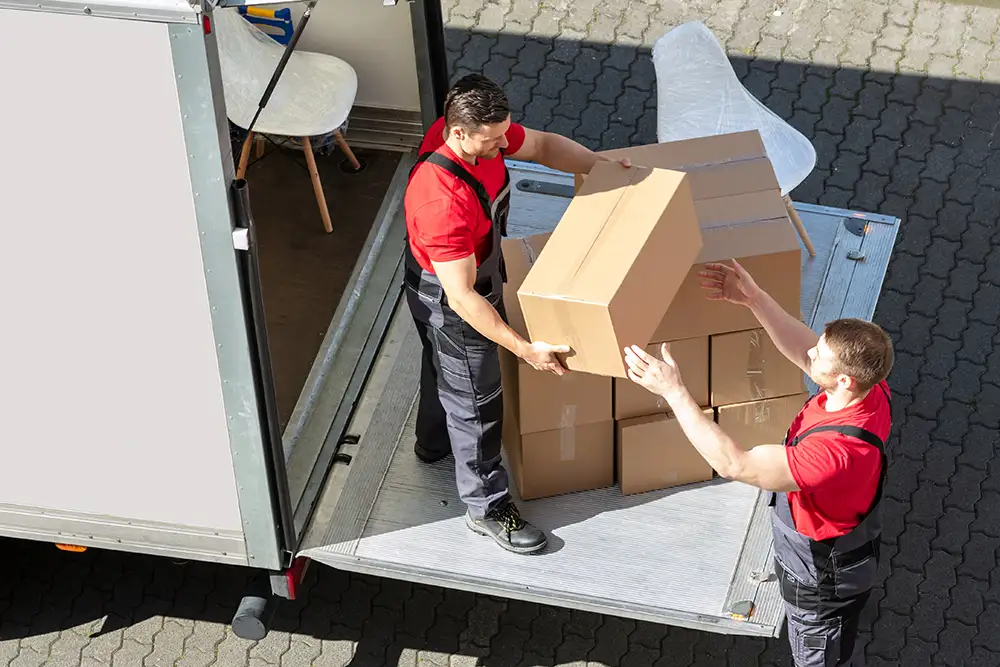 Männliche Umzugshelfer laden die Kartons vom LKW ab.